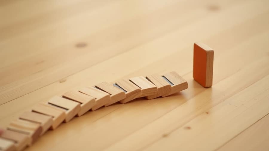 Geschwungene Kette aus Holz-Dominosteinen auf einem Holztisch, ein Stein in Orange